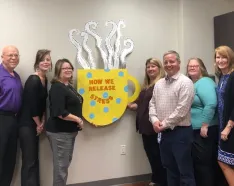 Seven EAP staff standing beside a cardboard cutout of a coffee cup