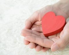 two hands holding wooden red heart