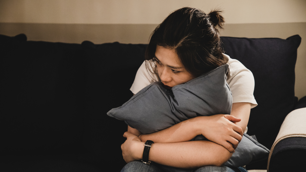 Sad woman sitting on couch hugging a pillow