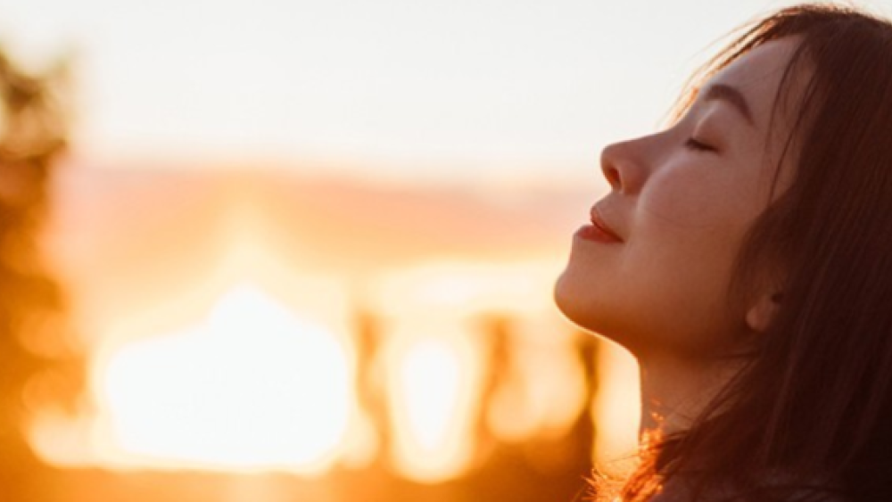 Woman Smiling with her eyes closed in front of a sunset