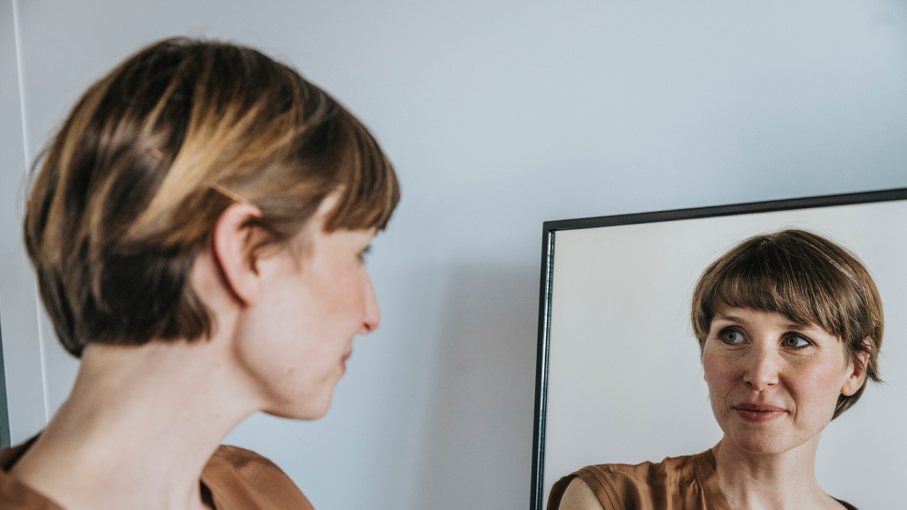 Thoughtful woman looking at reflection in mirror