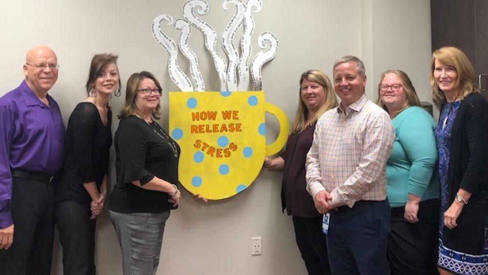 Seven EAP staff standing beside a cardboard cutout of a coffee cup