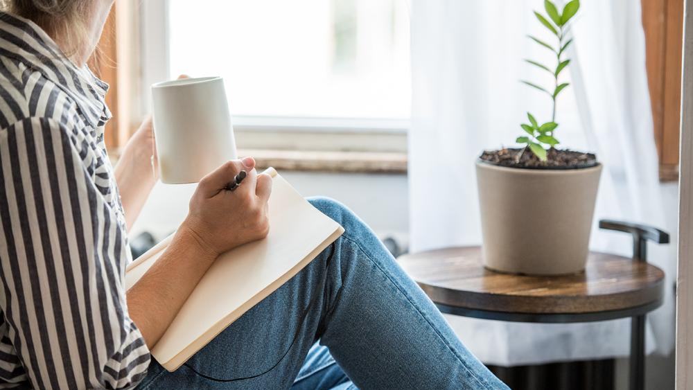 sitting woman having coffee writing in a notebook