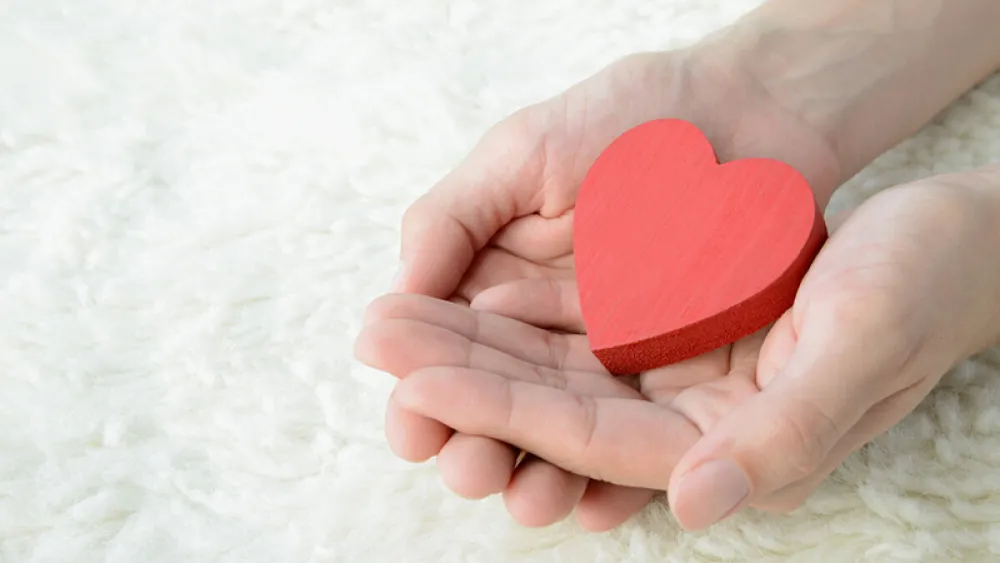 two hands holding wooden red heart